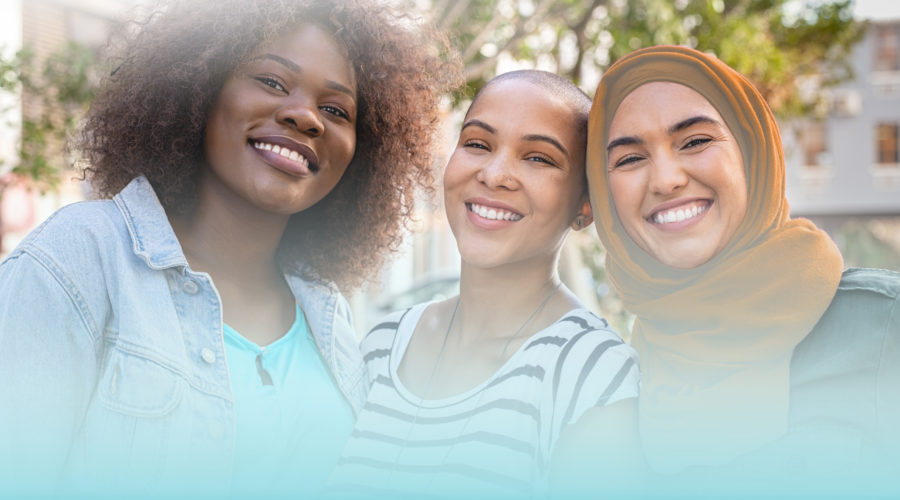 Group of three happy multiethnic friends looking at camera. Portrait of young women of different cultures enjoying vacation together. Smiling islamic girl with two african american friends outdoor.