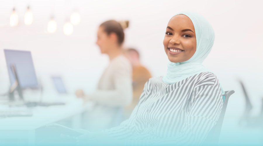 African american muslim girl with hijab working on a tablet in modern office. Caucasian girl and boy colleagues in the background