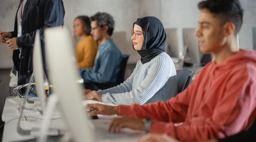 Female Muslim Student in Hijab, Studying in University. She Works on Desktop Computer in College with Diverse Multiethnic Classmates. Applying Her Knowledge to Acquire Academic Skills in Class.